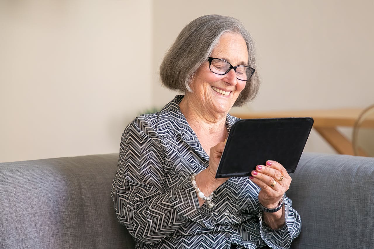 services-01 Happy senior woman with gray hair using a tablet at home, enjoying technology.