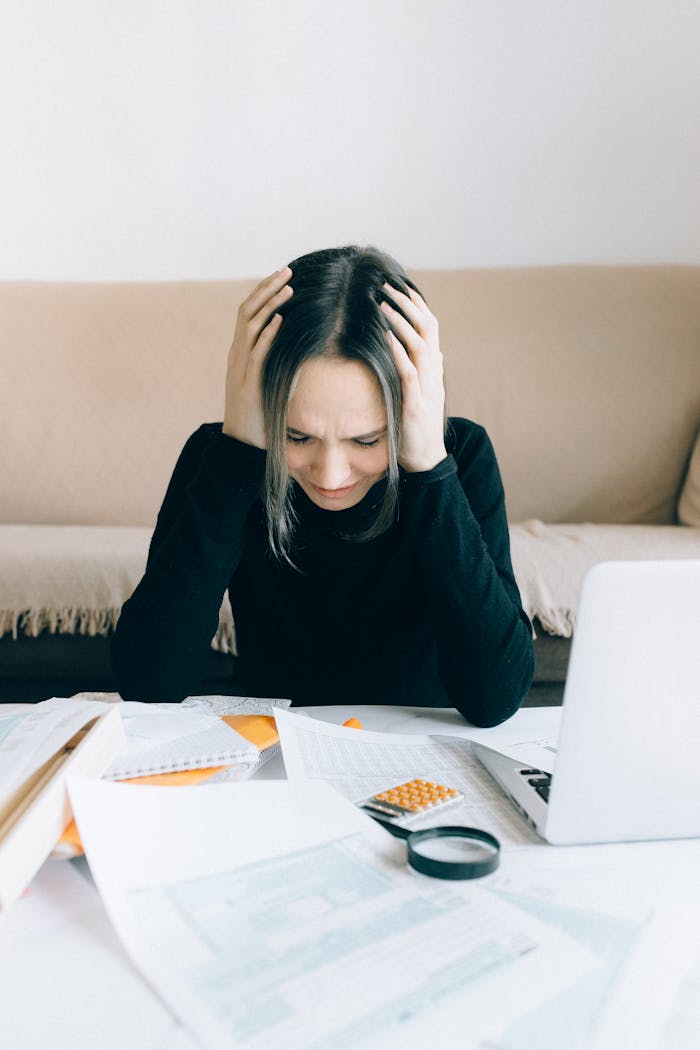 about-us A woman appears stressed and overwhelmed with paperwork at her home desk.